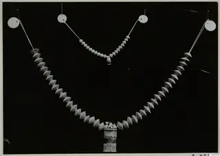 Two bead necklaces from Arsos, hung on pins from white discs against a black background