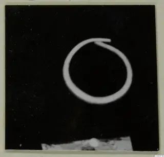 Single thin wire ring with overlapping ends against a black background, with a pale base along the bottom edge