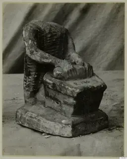 Limestone figure of a seated, headless person with one arm resting on a stepped base