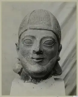 Limestone Neo-Cypriote head with a cross-hatched cap and large eyes, shown on a plain block base