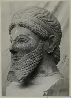 Limestone head of a bearded male figure with a leafy band around the crown, shown on a plinth against a draped backdrop.