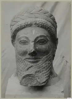 Limestone sculpted head of a bearded man in a band-and-leaf headdress, on a square base.