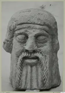 Limestone head of a bearded male figure from Soli, face and beard carved in relief.