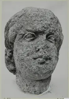 Stone head from Soli, a carved male or female face with hair framing it, shown against a pale background.