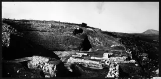 The theatre at Soli seen from the east, with rows of stone seating cut into a hillside and stone blocks in the foreground.