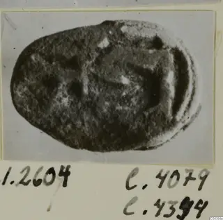 Oval dark stone seal or gem with a worn mottled surface, photographed on a card mount with handwritten labels.