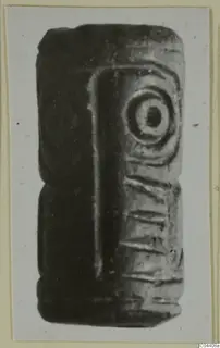Dark stone seal, rectangular and elongated, with a concentric circle motif and incised lines on its faces.