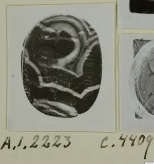 Oval engraved seal or gem with pale curved bands, shown on a card alongside other photographs.
