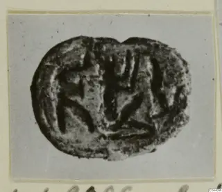 Glyptic: a dark oval seal with an incised linear design, shown in a photograph on a grey card mount
