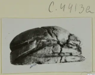 Dark stone object, possibly a seal or gem, with horizontal ridges and a crack, photographed on a mounted card