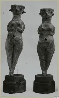 Two standing female figurines from Enkomi with hands on their chests, shown on wooden bases