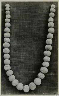 Necklace of pale, round beads laid in a U-shape on a dark cloth.