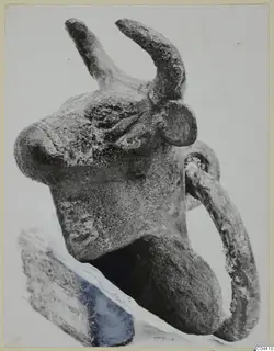 Bronze bull's head with curved horns and a loop at its side, resting on a dark stone block