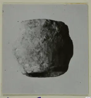 Blurred photograph of a small, rounded lead object on a grey card