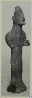 Terracotta figurine of a standing figure with a tall pointed head and arms bent at the sides