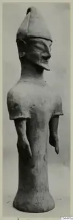 Terracotta standing figure with a tall pointed headdress and bent arms, photographed against a grey background