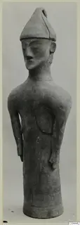 Terracotta figure from Ayia Irini with a pointed cap, long face and arms held at the sides, shown against a plain backdrop