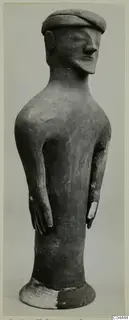 Terracotta figure of a standing human figure with a flat cap-like head, long neck and arms held at the sides.