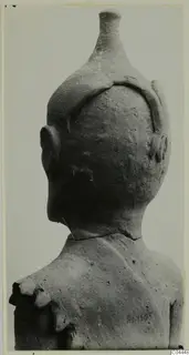 Back view of a terracotta figurine's head and shoulders, with a tall tapering headdress and rounded ears.