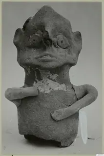 Terracotta figurine with a pointed head, modelled eyes and mouth, and two short arms, shown against a grey background.