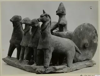 Terracotta group of four animal figures harnessed to a cart with a disc wheel and a standing human figure, on a flat base