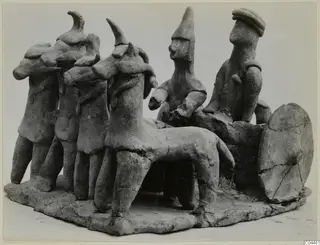 Handmade terracotta group of small figures, some with animal-like heads, beside a standing quadruped on a flat base.