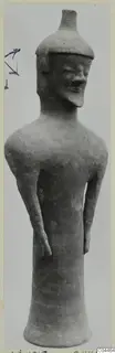 Terracotta standing figure with a flat-topped cap, bent arms at the sides and a flared base, against a grey backdrop.