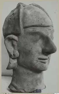 Terracotta head with a tall flat-topped cap, long nose and large ear, photographed against a grey backdrop