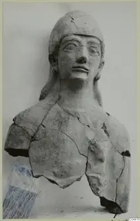 Broken terracotta bust of a figure with a rounded headdress and cracked surface, against a plain background