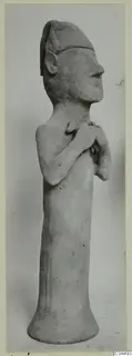 Terracotta figurine of a standing figure with a flat cap and hands clasped at the chest, shown in side view.