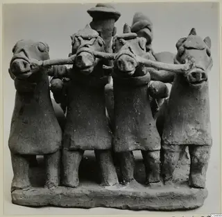 Terracotta group of four small standing figures with animal-like heads, arms linked, on a rectangular base