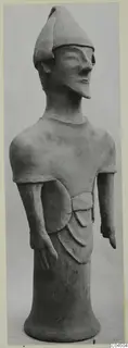 Standing terracotta figure wearing a pointed cap, arms at its sides, shown against a plain grey background