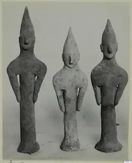 Three terracotta figurines of standing figures with tall pointed heads and arms held at their sides.