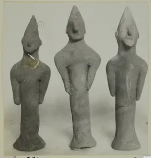 Three terracotta figurines of standing figures with pointed heads and long necks, shown side by side.