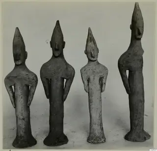 Four terracotta figurines standing in a row, with tall pointed heads and elongated bodies.