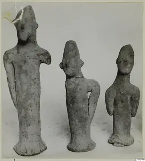 Three terracotta figurines of standing human figures shown side by side against a plain grey backdrop.