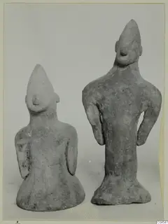 Two small terracotta human figurines with pointed heads and flared bases, standing side by side.