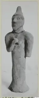 Terracotta figurine of a standing human figure with a pointed head covering and one hand raised to the chest, from Ayia Irini