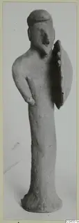 Terracotta figurine of a standing human figure with a flat-topped head and a flat oval piece at its side.