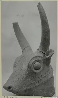 Terracotta animal head with two long curved horns, a round eye boss and rows of small impressed dots on the face