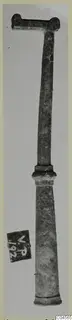 Long bronze tool with a T-shaped top and tapering shaft, photographed upright against a plain background.