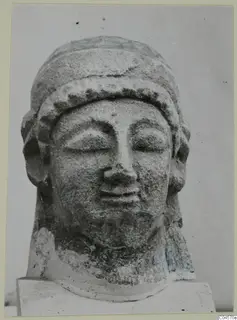 Limestone head of a figure with closed eyes, a band across the forehead and hair at the sides.