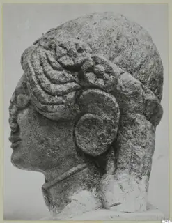 Limestone head of a statue from Arsos, shown in side profile with elaborate curled hair and a large ear ornament.