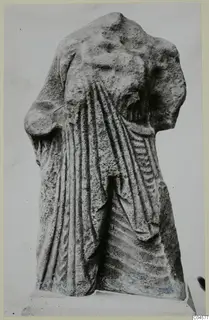 Limestone statue fragment from Arsos, headless and armless, with drapery folds, standing on a plinth.
