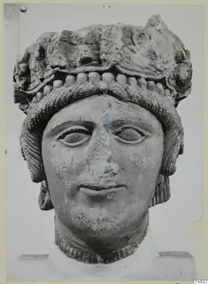 Limestone head of a figure wearing a high headdress, photographed frontally against a plain background.