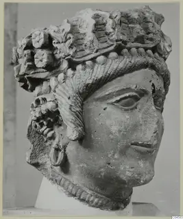 Carved limestone head from Arsos, with a high headdress of rosettes, leaf forms and ridged bands
