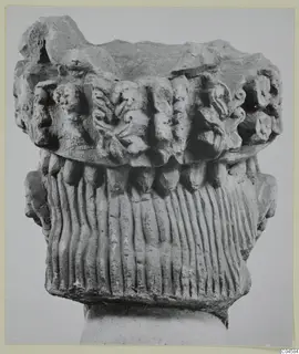 Carved limestone capital from Arsos, with leaf-like carving above a fluted section, shown on a plain block