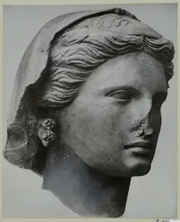Stone sculpture of a female head with wavy hair and a veil, a cluster-shaped earring, and a chipped nose.