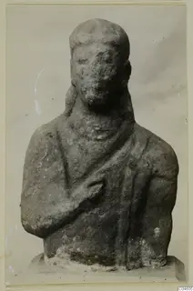 Limestone Proto-Cypriote bust with one arm bent across the chest and a worn, pitted face