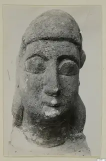 Close-up of a limestone head sculpture with a flat-topped headdress and large almond-shaped eyes